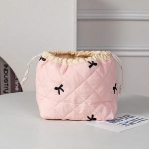 Detailed view of pink quilted cosmetic bag with black embroidered bows and drawstring closure