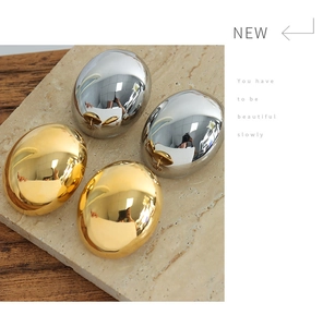 Close-up of polished gold and silver oval hoop earrings on a stone display tray