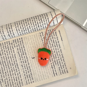 Close-up of a plush strawberry charm with embroidered face on an open book background
