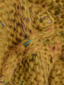 Macro shot of chunky space-dye knit fabric in mustard yellow with multi-color fibers