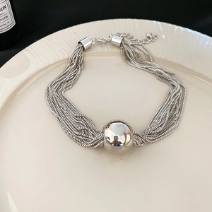 Detail of silver multi-layered chain bracelet with a central metal bead on a white plate