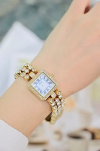 Elegant gold square watch with rhinestones worn on wrist with Roman numerals