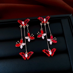 Macro shot of long gold earrings with butterfly design and red stones on black velvet