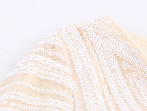 Macro shot of elegant white sequins embroidered on beige mesh fabric with wavy patterns