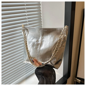 Detail of silver metallic bucket bag featuring a gold woven chain strap held by model