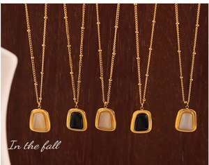 Detail of gold bead chains with opal-like rectangular pendants on wood background
