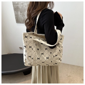 Detailed close-up of a beige corduroy tote bag with black bow pattern on model shoulder