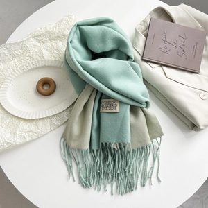 Detail shot of mint green cashmere-style scarf with fringe and woven label on a table