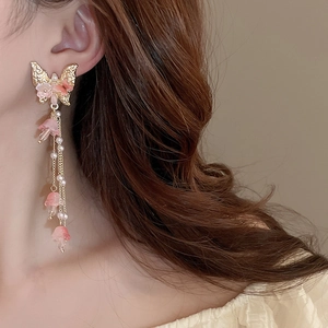 Détail de boucles d'oreilles pendantes dorées avec papillon et fleurs roses
