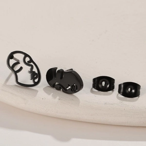 Close-up of black minimalist abstract face earrings on a textured ceramic dish