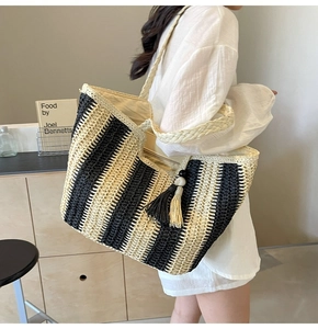 Detail shot of a large striped straw tote bag with tassel charm and zipper closure