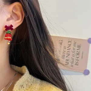 Detailed view of handmade beaded Christmas tree earrings with red velvet bow and golden bell