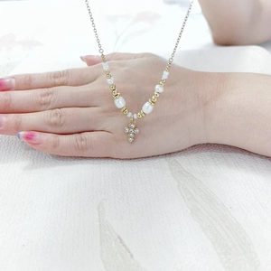 Detail of gold cross pendant with clear crystals and white pearl strand necklace