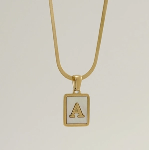 Detailed view of golden square pendant with white shell inlay and letter A on snake chain