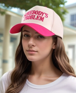 Detail of pink and white baseball cap with Somebody's Problem embroidery on cotton fabric