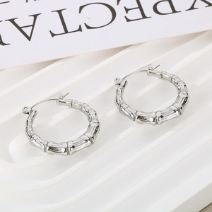 Detail of silver bamboo textured U-shaped hoop earrings on a white wavy pedestal