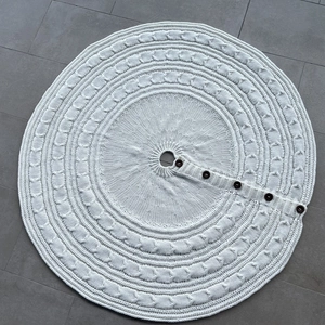 Detail of white cable knit Christmas tree skirt with wooden button closures on grey floor