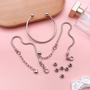 Flat lay of silver DIY bracelet set with heart pendants and beads on pink background
