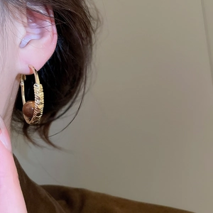 Detailed close-up of textured golden hoop earrings with brown bead on ear model
