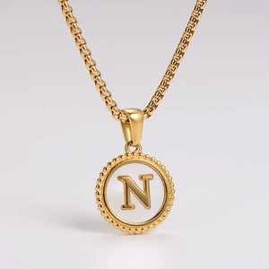 Macro shot of gold necklace with a round shell pendant featuring a raised letter N detail