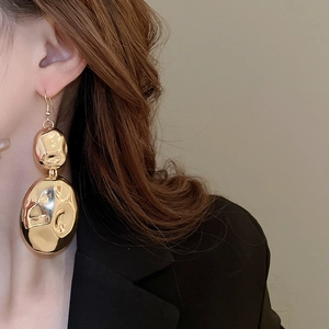Detailed view of gold crinkled metal earrings worn by a model to show texture