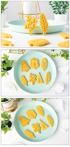 Detailed view of yellow Christmas tree shaped cookie cutters and pressed fondant leaf shapes