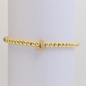 Macro detail of gold beaded bracelet featuring a shimmering zircon-paved letter J charm