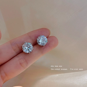 Macro shot of silver six-prong cubic zirconia studs held by fingers against silk background