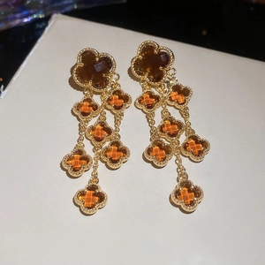 Macro detail of gold plated four-leaf clover drop earrings with amber crystal inlays