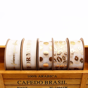 Five rolls of white and gold organza ribbons with letter patterns in a wooden box