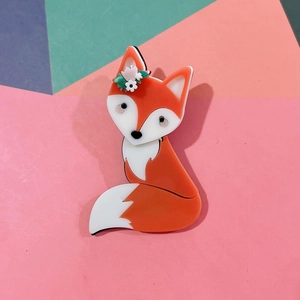Macro detail of cute acrylic orange fox brooch with green flower on a colorful background