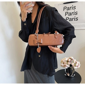 Close-up of brown vintage baguette bag with bow and heart pendants on leather