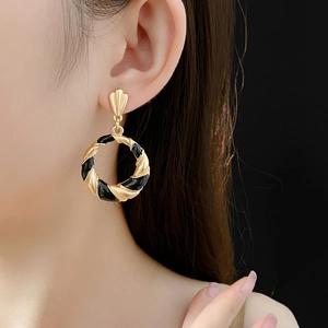 Detailed view of a model wearing vintage twisted golden hoop earrings with black enamel