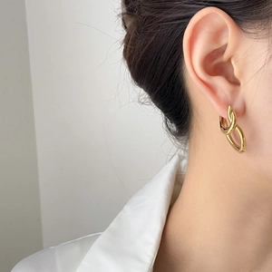 Detail of interlocking gold geometric oval hoop earrings worn by a model in soft light