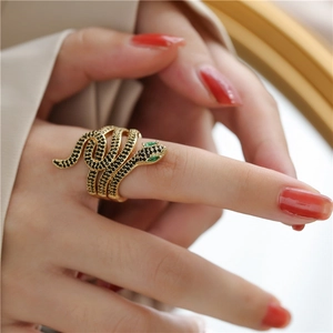 Close-up of golden snake ring set with black stones and green gemstone eyes on hand