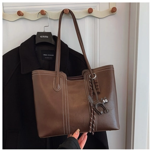 Detail of dark brown tote bag with white contrast stitching and cat shaped charm