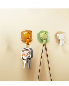 Detail of four colorful cat-ear adhesive wall hooks with golden rings and clear backing