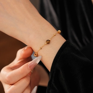 Detailed view of a gold-plated bracelet with a round tiger eye stone on a model's wrist