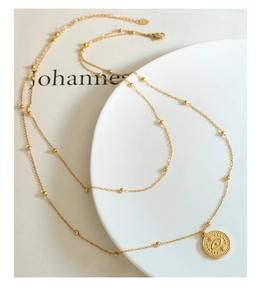 Detail of 18k gold plated double layer necklace with Evil Eye coin pendant on white tray