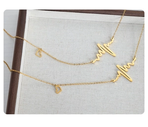 Detailed view of two gold heartbeat necklaces with mini heart pendants on linen