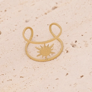 Détail de bague double couche en acier doré avec motif soleil et texture sur fond pierre