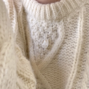 Macro shot of silver S925 oval Virgin Mary pendant necklace on white knit sweater