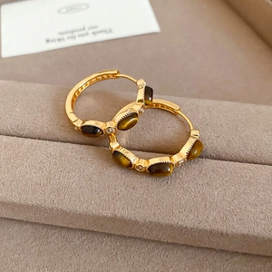 Close-up of gold plated hoop earrings with brown tiger eye stone and zircon accents