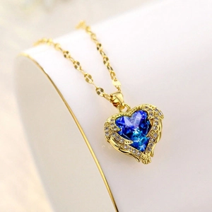 Macro shot of gold heart pendant with faceted blue gemstone and sparkling wings