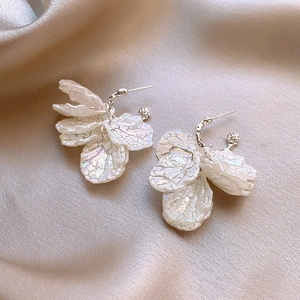 Détail de boucles d'oreilles fleur nacrée à pétales superposés sur soie couleur champagne