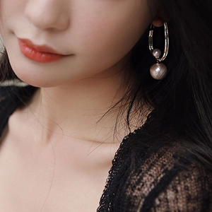 Close-up of elegant C-shaped gold pearl earrings with zircon on a female model's ear