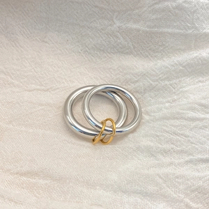 Detail of overlapping silver and gold double loop ring on white textured fabric