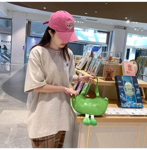 Detail of green canvas tote bag with funny expression held by model wearing pink cap