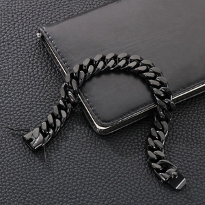 Detail view of a black Cuban link bracelet with clasp resting on a dark textured surface