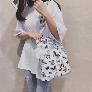 Detailed shot of a white canvas tote bag with butterfly prints and a plush bear charm